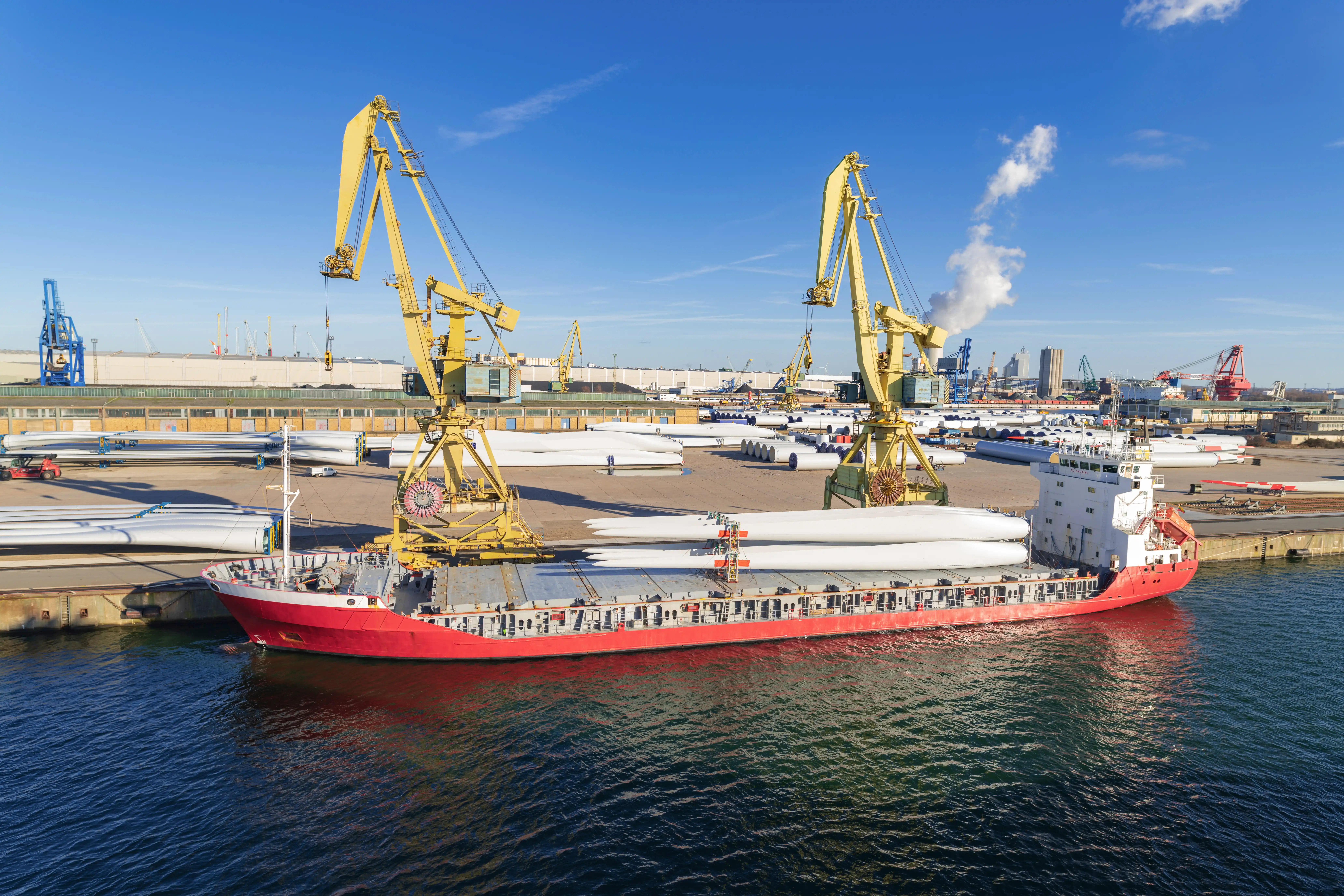 Schiff mit gelben Kränen im Hafen, beladen mit langen Windkraftflügeln Schiff mit gelben Kränen im Hafen, beladen mit langen Windkraftflügeln