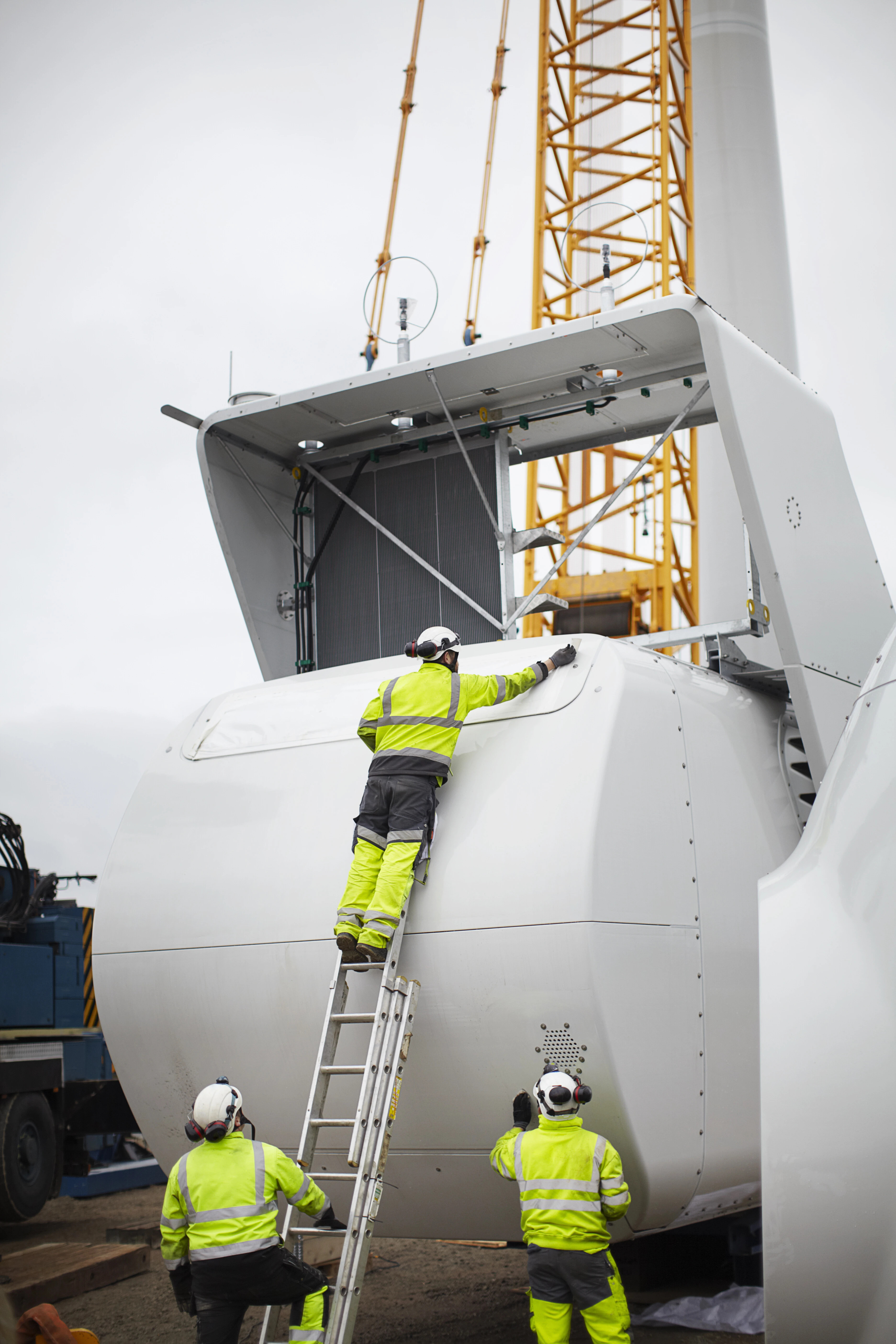 Arbeiter in Schutzkleidung bei der Demontage einer Windkraft-Gondel, mit Kran im Hintergrund